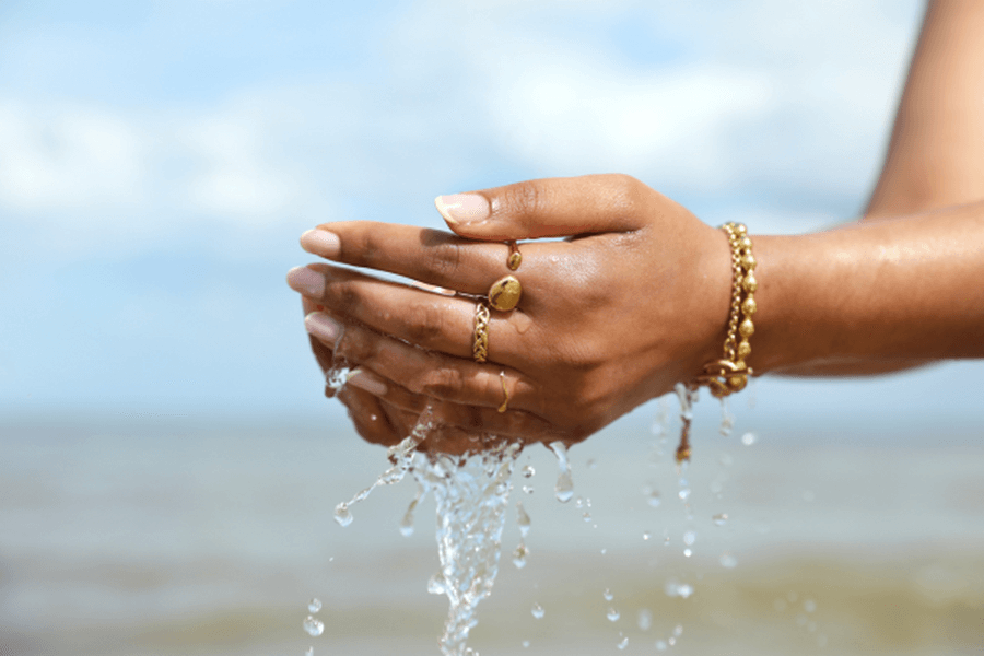 Hands holding water, showcasing waterproof jewellery care in a natural setting by the sea.